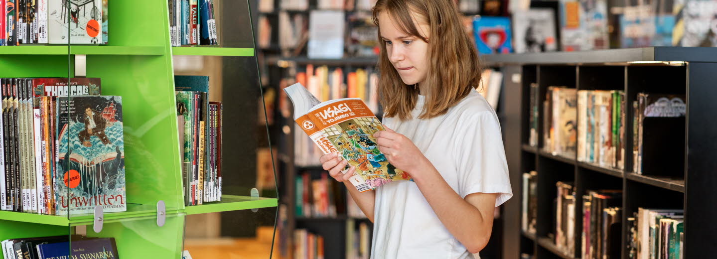 Flicka läser en bok på ett bibliotek.