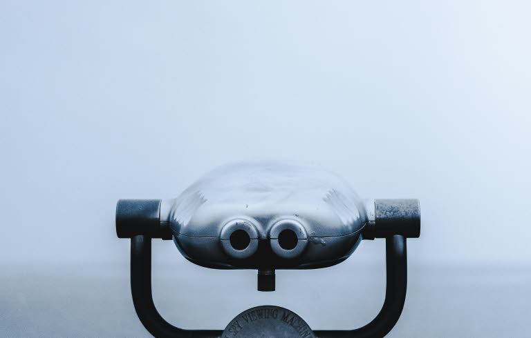 Foto av en kikare i fören på en båt. Dimmigt hav i bakgrunden. 