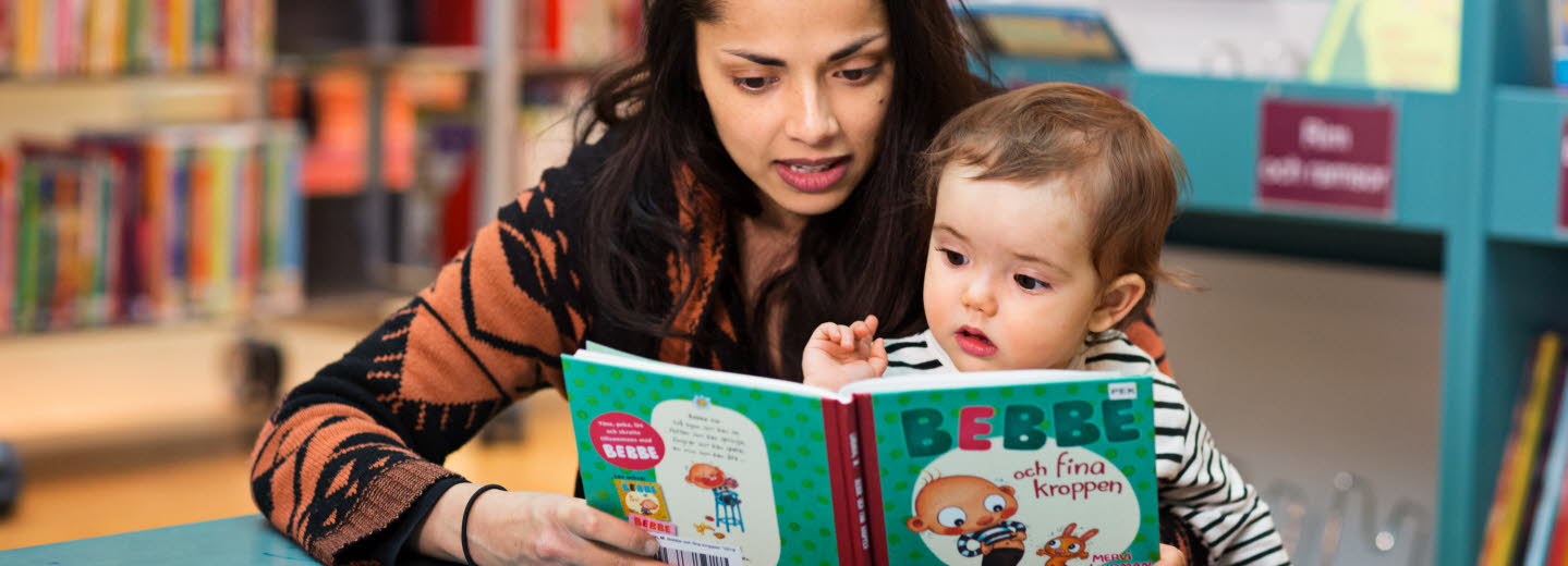 Kvinna och barn sitter vid ett litet bord på ett bibliotek och titta i en pekbok.
