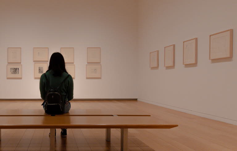 En kvinna som sitter på en bänk och tittar på konst i en utställningshall.
