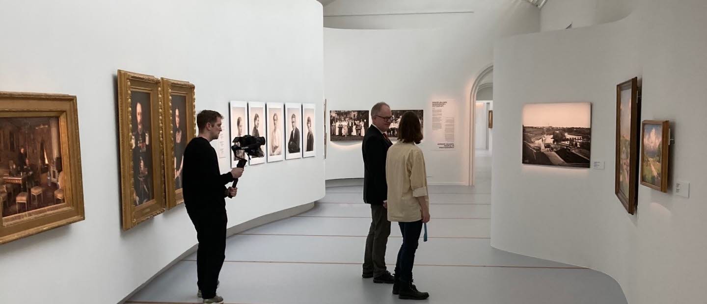 Två personer tittar på konst på Östergötlands museum. I bakgrunden står en filmare och filmar.