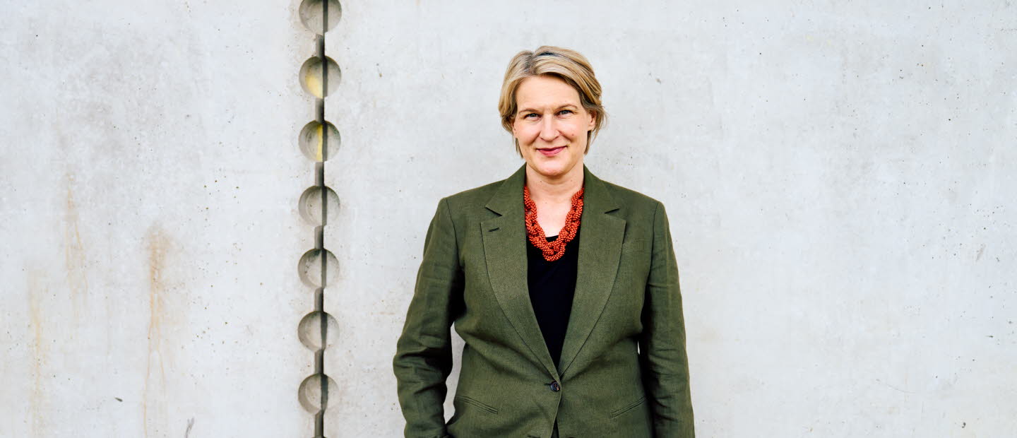 Pressbild på Kajsa Ravin som står framför en grå vägg.