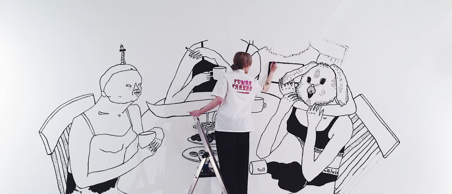 Bim Eriksson is painting on a wall. She's painting four women sitting att a dinner table.