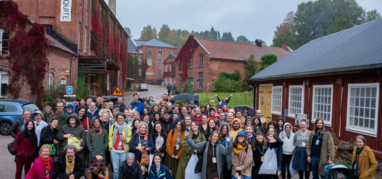 Gruppbild utomhus. I bakgrunden syns ett rött trähus och flera tegelhus.
