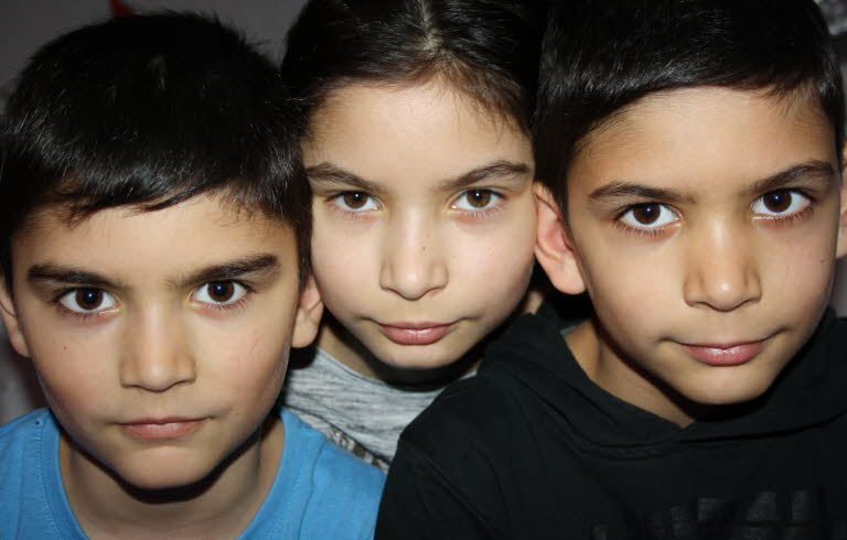 Foto på tre barn, de tittar in i kameran med skarp och nyfiken blick.