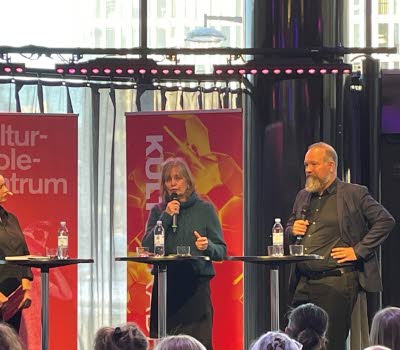 En man och en kvinna på en scen med ståbord och röd bakgrund