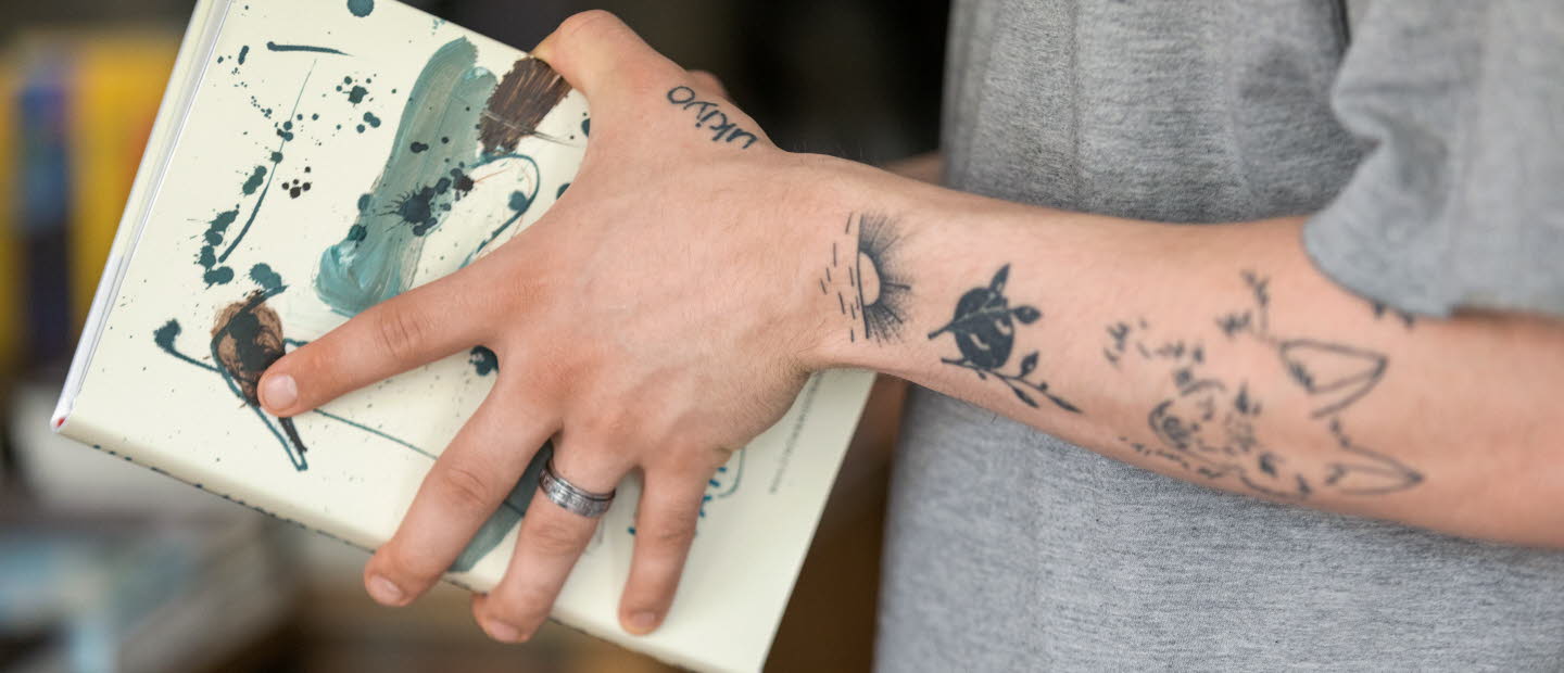 Tatuerade armar som håller i en bok.