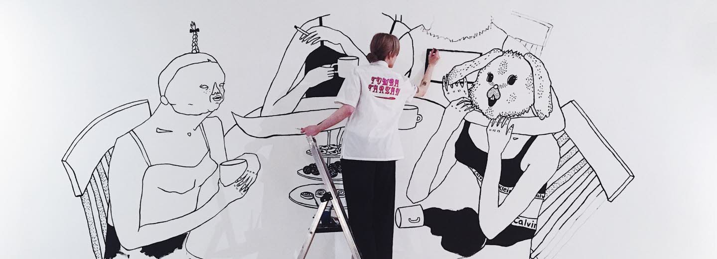 Bim Eriksson is painting on a wall. She's painting four women sitting att a dinner table.