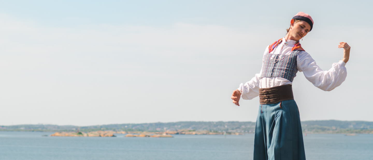 Person i folkdräkt står på en klippa vid havet med öar i bakgrunden.