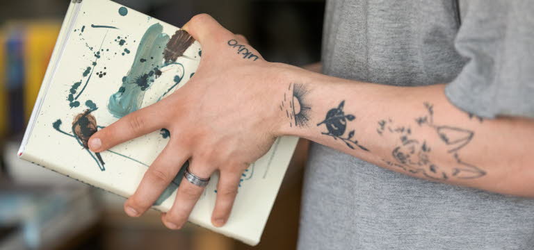 Tatuerade armar som håller i en bok.