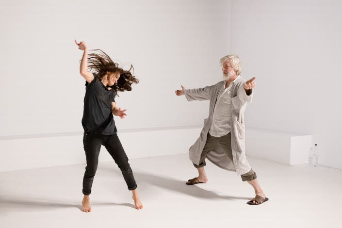 A young woman and an old man are doing a modern dance in a white room.