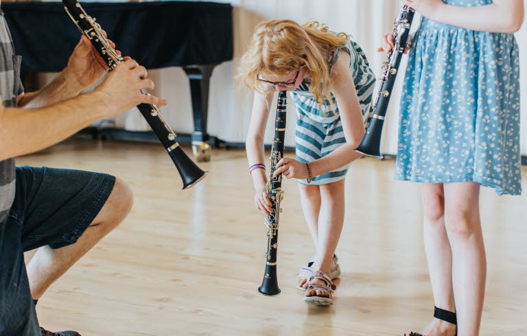 Barn spelar blåsinstrument tillsammans med en vuxen.