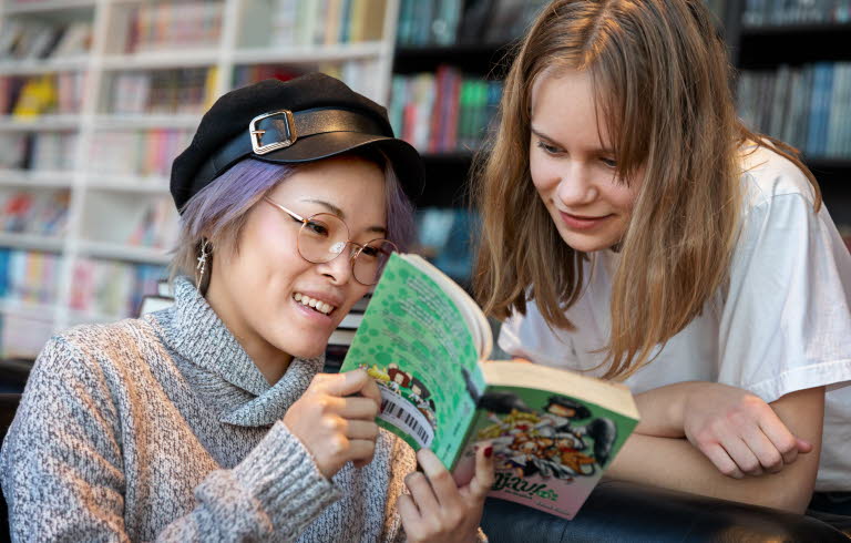 Två ungdomar på ett bibliotek tittar i en bok tillsammans