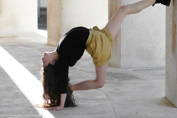 Akrobatisk dansrörelse av Marina Cherry med foten mot en betongpelare.