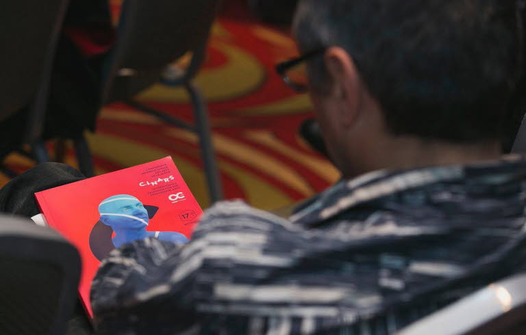 Foto av en man bakifrån som sitter och tittar på programmet för Cinars. Omslaget är rött med en blå man från axlarna och uppåt.