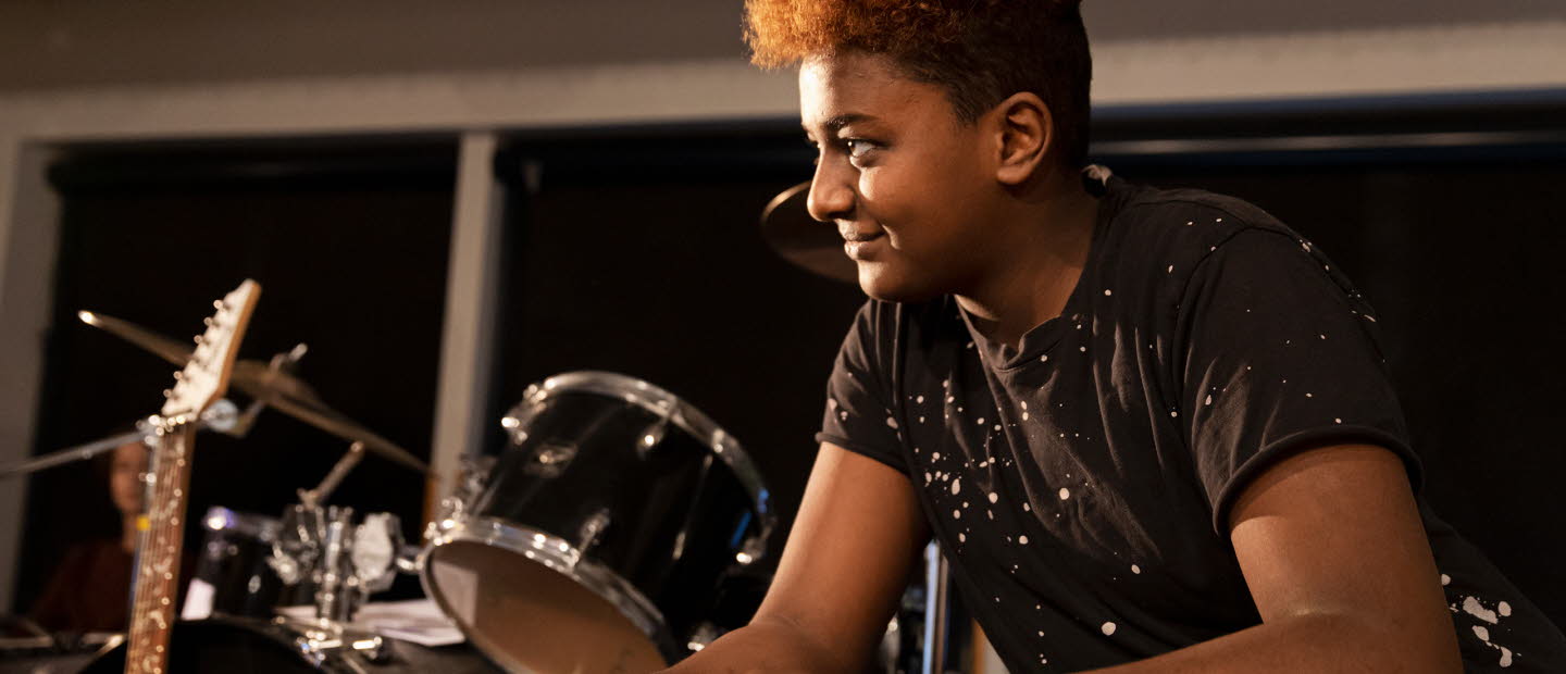 En ung man som sitter vid ett trumset och ler.