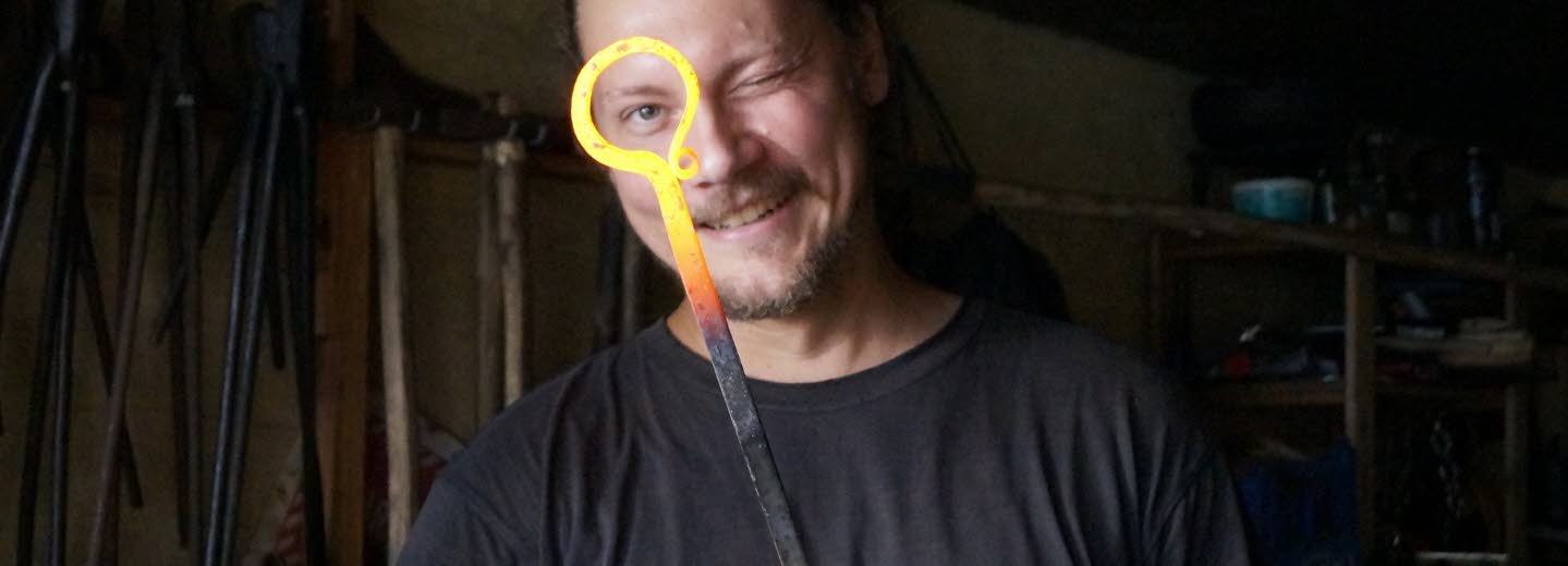 Smed i verkstad som håller ett glödhett smidesjärn.