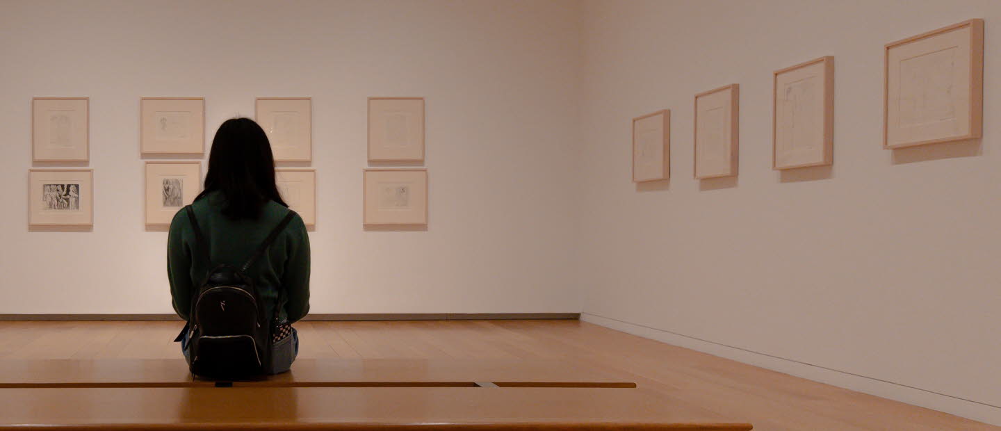En kvinna som sitter på en bänk och tittar på konst i en utställningshall.