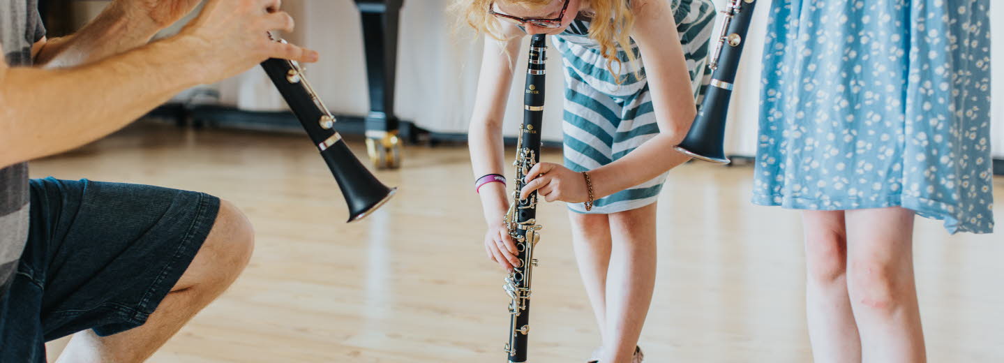 Barn spelar blåsinstrument tillsammans med en vuxen.