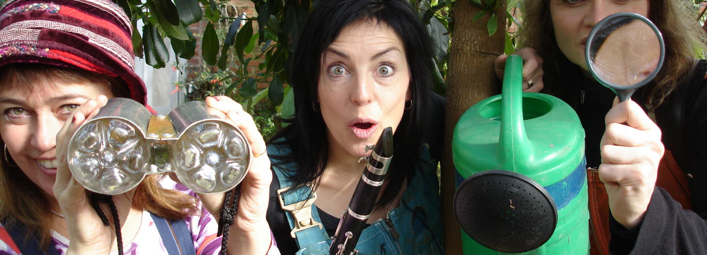 Tre personer står bland träd och tittar nyfiket in i kameran. De håller i en vattenkanna, en flöjt och en kikare.