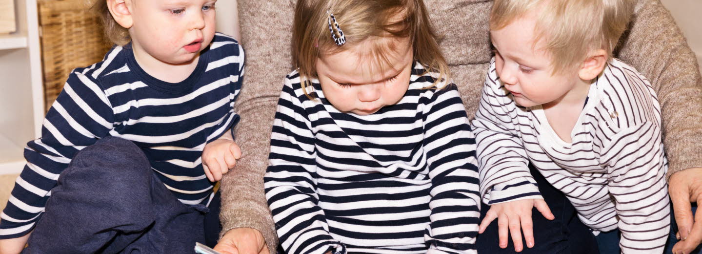 Tre barn som sitter på golvet och bläddrar i en bok. 