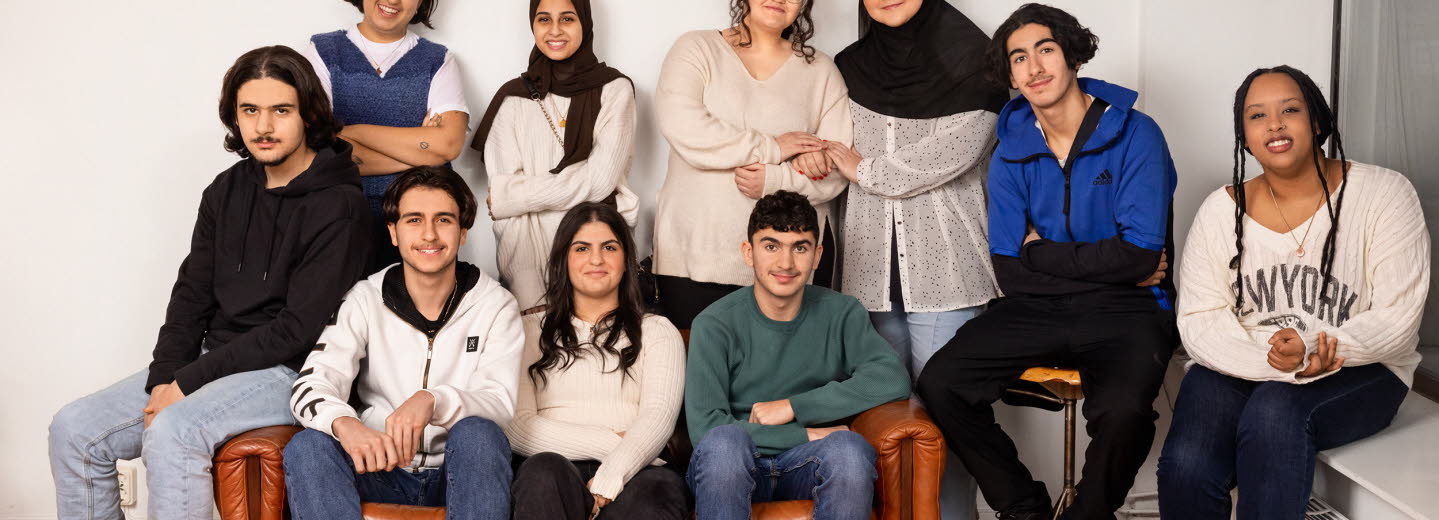 Gruppbild: En kvinna och nio ungdomar - både pojkar och flickor. Gruppen har trängt ihop sig i ena hörnet av ett rum och är samlade kring en soffa.
