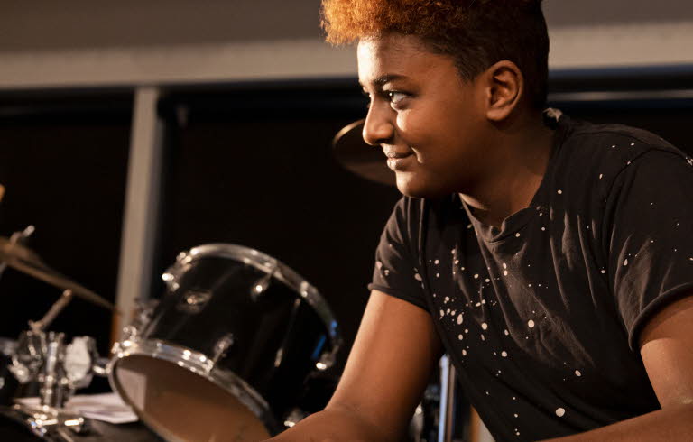 En ung man som sitter vid ett trumset och ler.