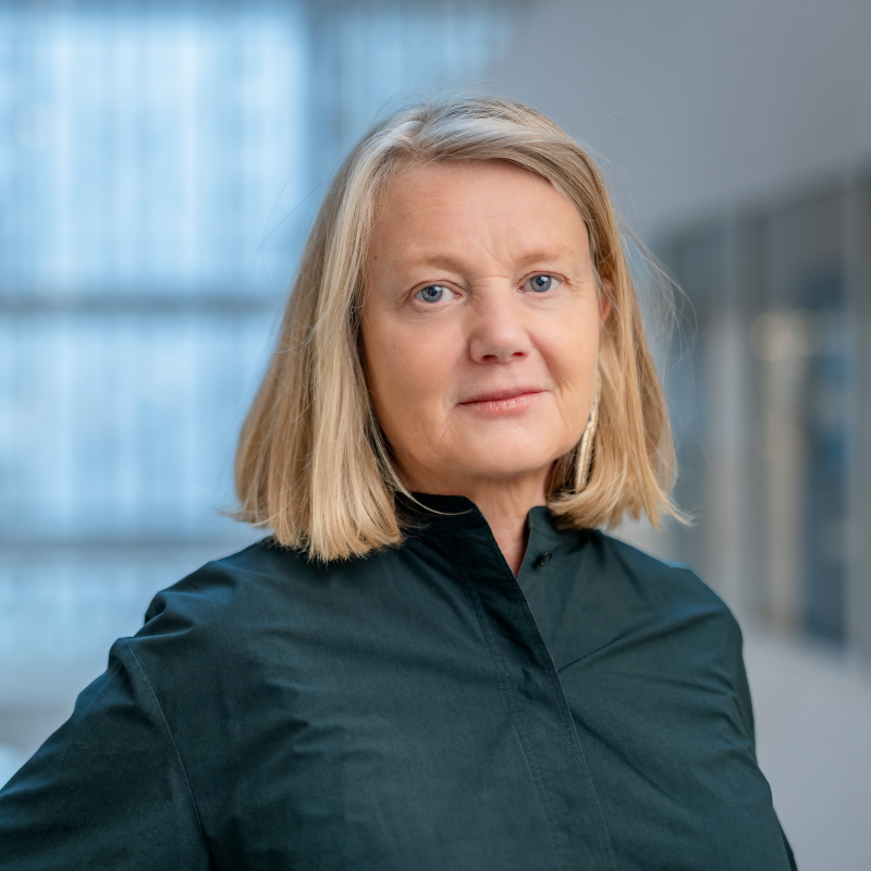 Medelålderskvinna i halvfigur. Blond page och mörkblå blus. 