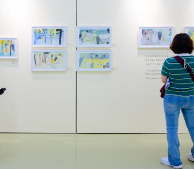 Tre personer tittar på en utställning med teckningar av Eva Lindström under Jeonju internationella bilderboksmässa 2025. Three people are viewing an exhibition of drawings by Eva Lindström at the Jeonju International Picture Book Fair 2025.