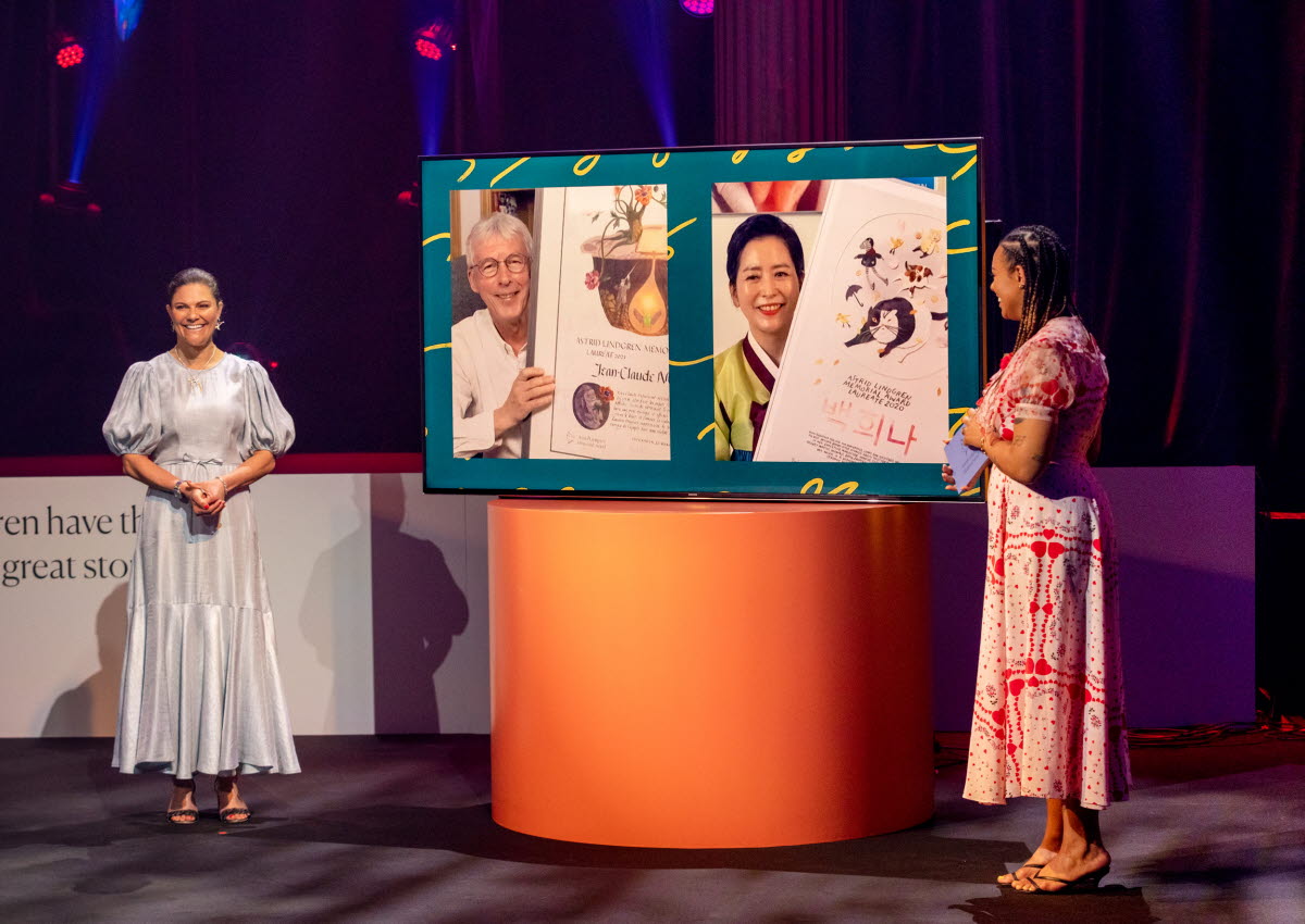 The princess of Sweden, Victoria is standing on stage with an other woman who we only see the back of. They are wearing festive dresses. 