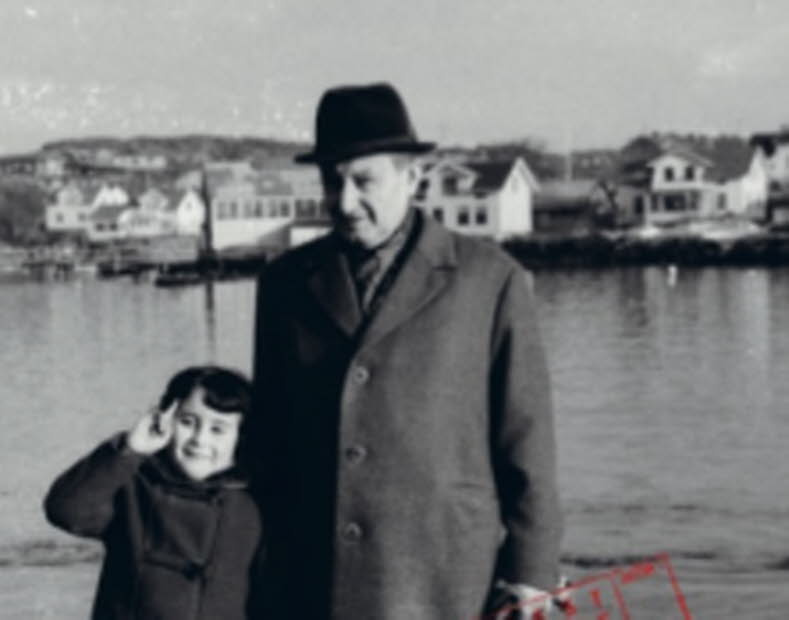 Book cover: A photo of and old man who's holding a child's hand. They are stadning infront of water, and on the other side of the water there's some houses.