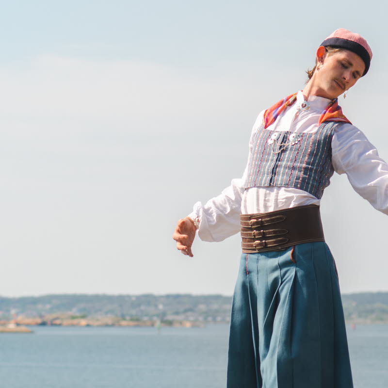 Person i folkdräkt står på en klippa vid havet med öar i bakgrunden.