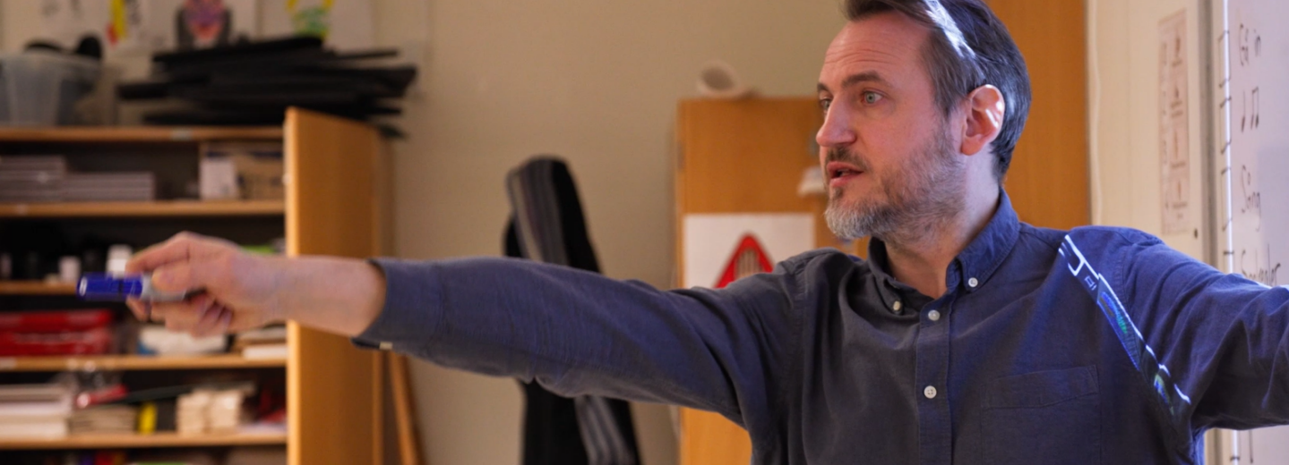 Manlig lärare pekar med en penna i ett klassrum.