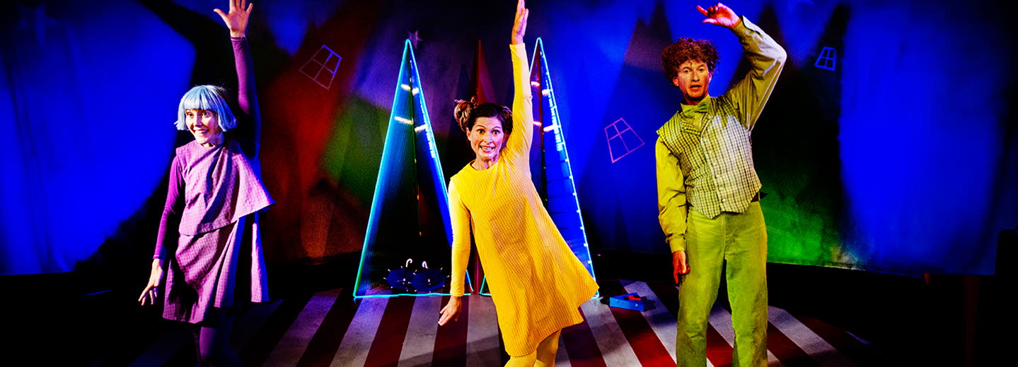 Tre vuxna som mimar och dansar. Färgstark scenografi med bredrandigt golv och blåbelysta väggar.