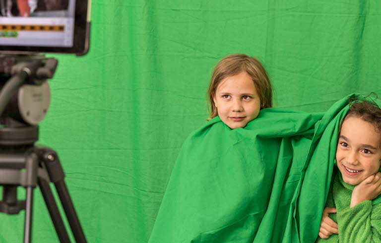 Två barn med gröna kläder blir filmade mot en grön vägg.