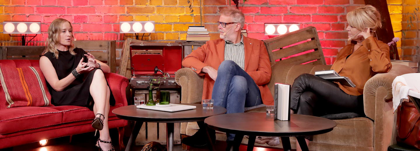 Three people are sitting and talking in a lounge setting.