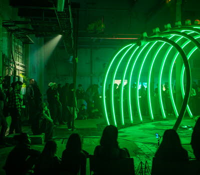 Publik står i ett mörkt rum runt ett uppbyggt stort skelett föreställande revben, skulpturen är upplyst med grönt ljus.