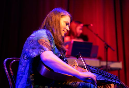Kvinna spelar nyckelharpa på en scen. I bakgrunden medmusikant på keyboard.