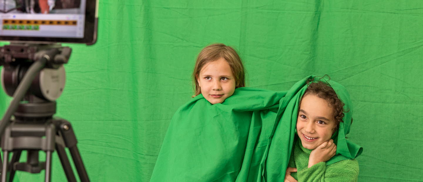 Två barn med gröna kläder blir filmade mot en grön vägg.