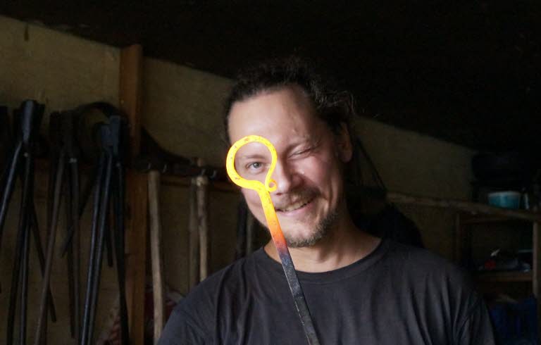 Smed i verkstad som håller ett glödhett smidesjärn.