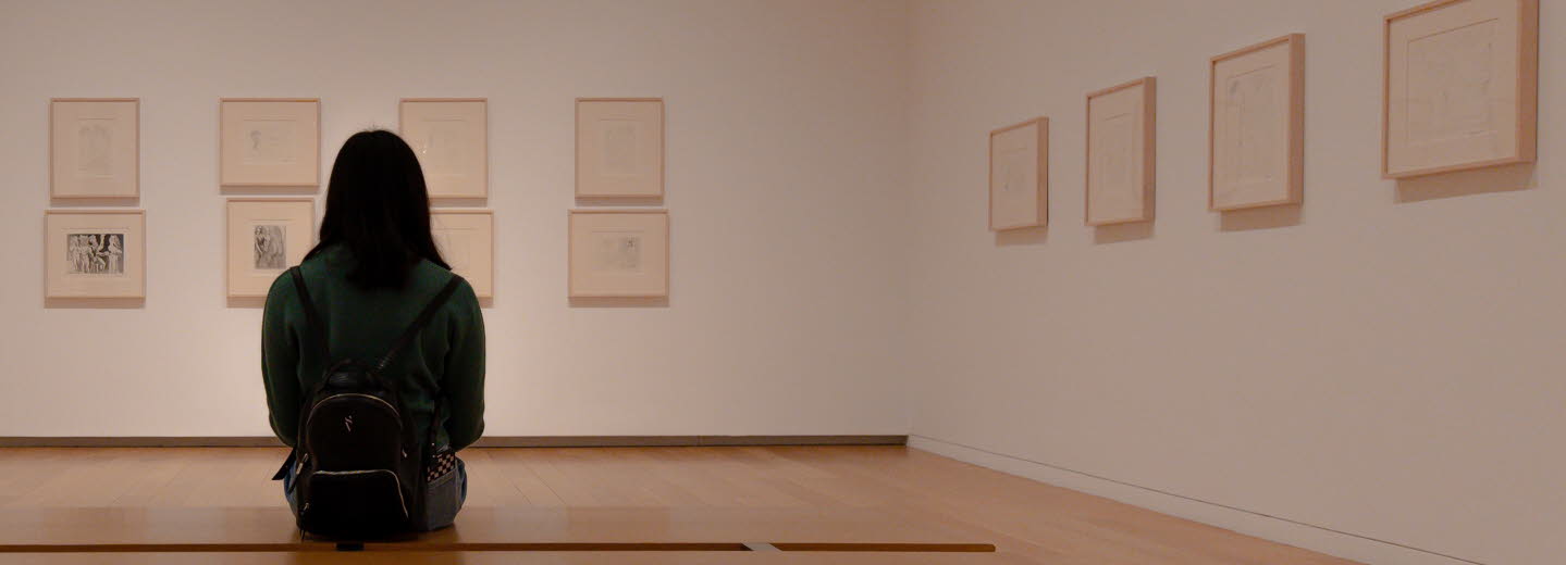 En kvinna som sitter på en bänk och tittar på konst i en utställningshall.
