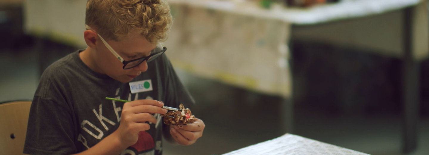 Pojke sitter vid ett bord och målar på figurer.