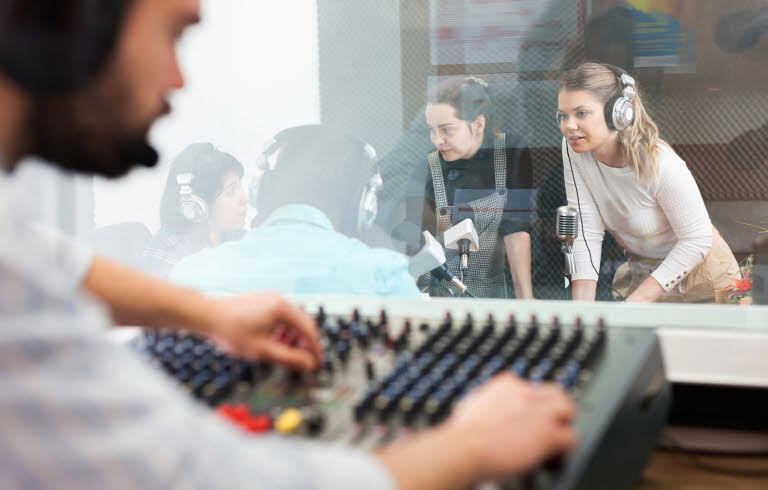 Radioinspelning. Man vid mixerbord och tre tjejer och en man samtalar med mikrofoner och headsets.