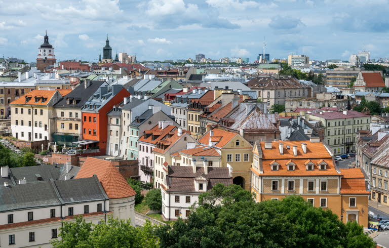 Bild över flera hustak i staden Lublin. I bakgrunden skymtas ett kyrktorn. Vädret är sol med växlande molnighet.