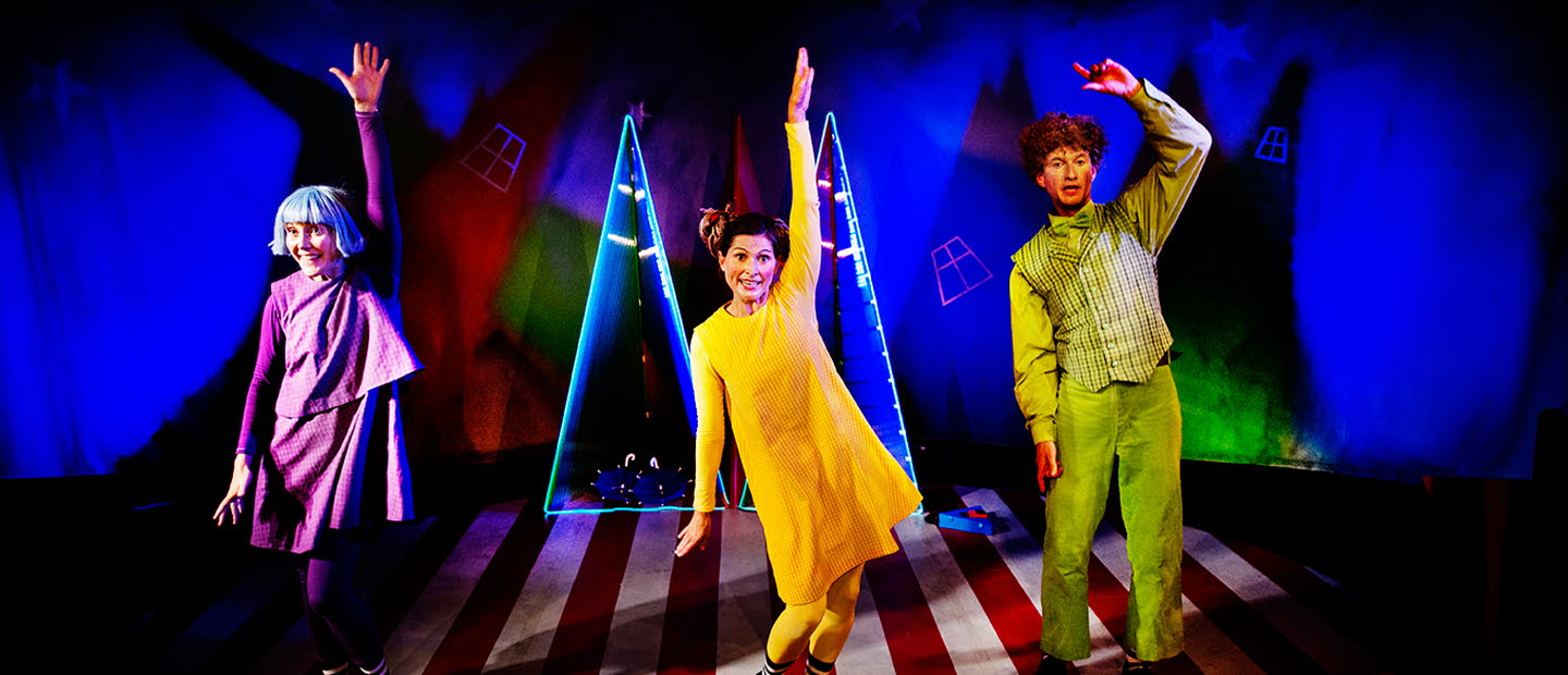 Tre vuxna som mimar och dansar. Färgstark scenografi med bredrandigt golv och blåbelysta väggar.