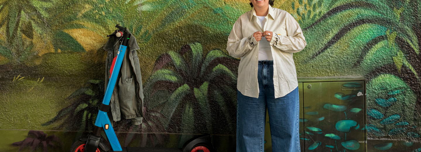 Läsambassadören Nioosha Shams med en sparkcykel framför djungelmålad vägg.