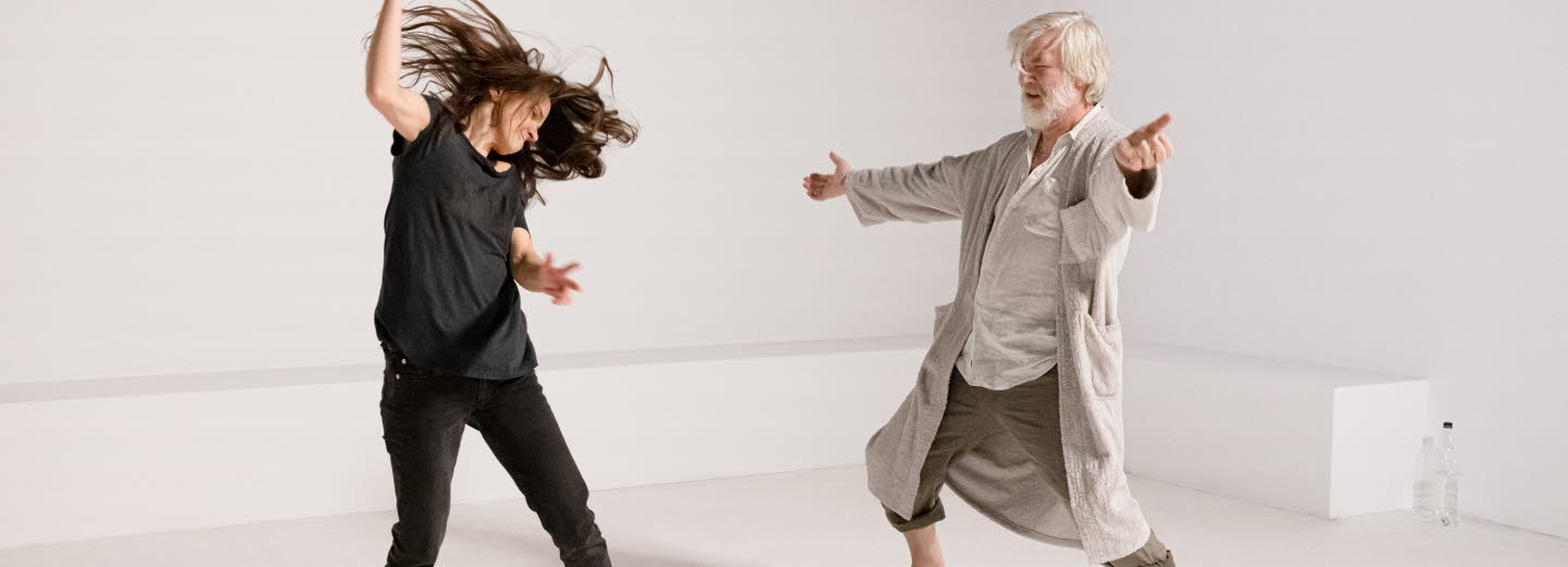 A young woman and an old man are doing a modern dance in a white room.