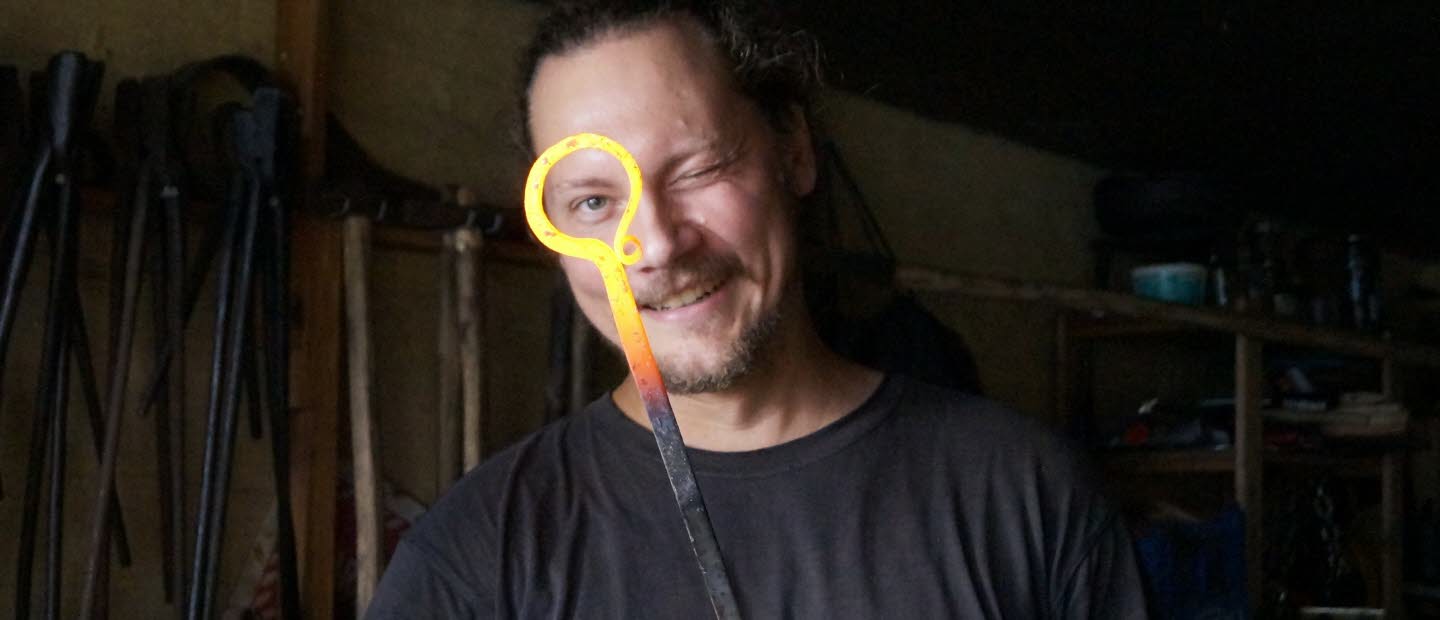 Smed i verkstad som håller ett glödhett smidesjärn.