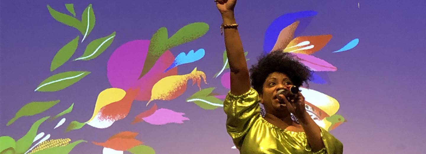 Kvinna som håller en mikrofon i handen och ströcker upp ena handen i luften.