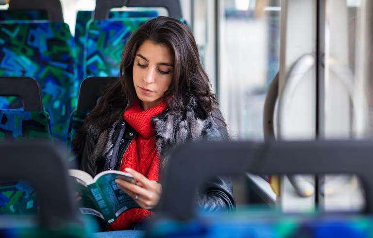 Kvinna på buss läser en bok.